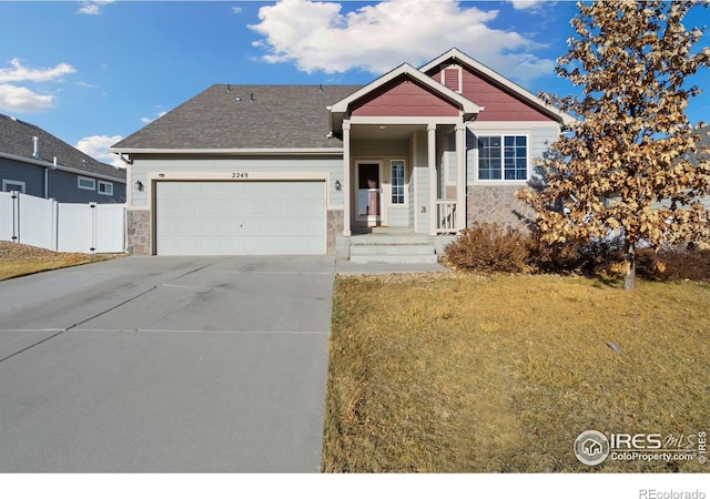 view of front of home featuring an attached garage, a front lawn, fence, stone siding, and driveway
