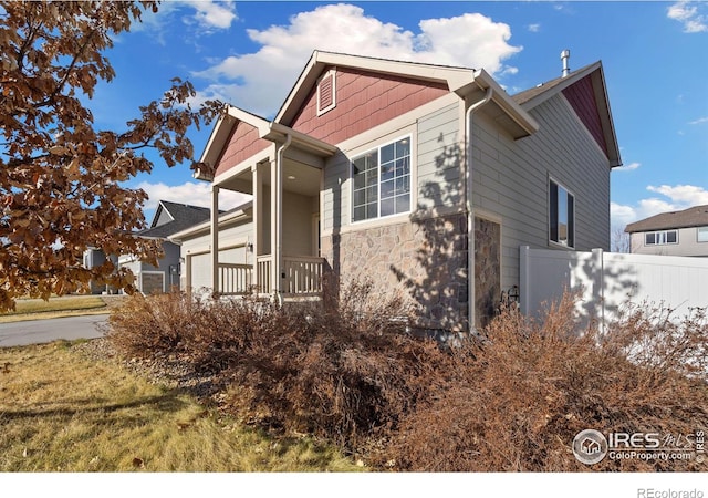 view of side of home with an attached garage, fence, and stone siding