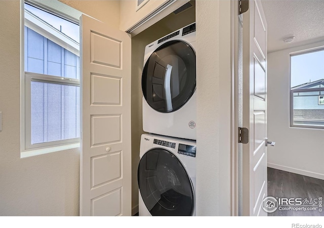 clothes washing area with baseboards, laundry area, dark wood-style flooring, stacked washer / drying machine, and a textured ceiling