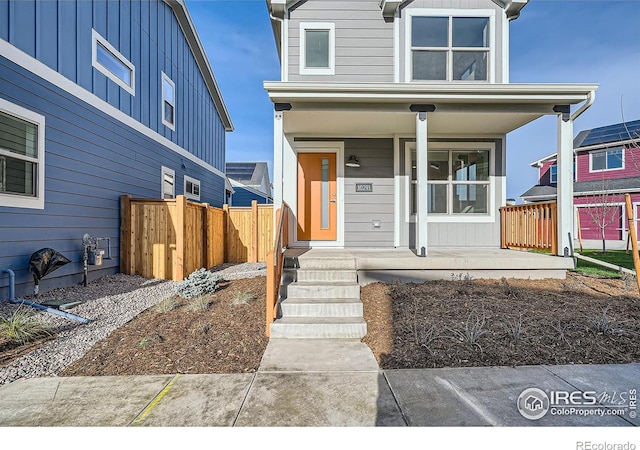 view of front of house with board and batten siding, covered porch, and fence