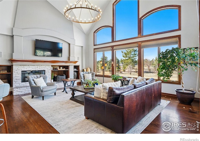 living room featuring a stone fireplace, hardwood / wood-style flooring, a notable chandelier, and high vaulted ceiling
