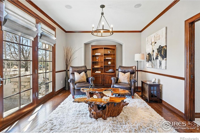 living area featuring a chandelier, baseboards, wood finished floors, and crown molding