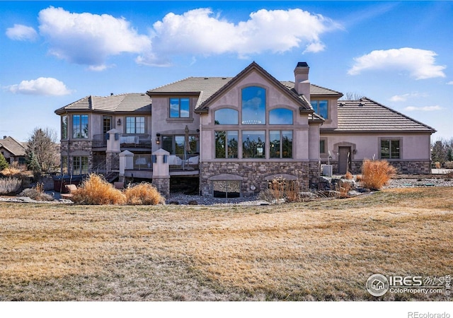 back of property with a yard, a chimney, stucco siding, stone siding, and a tiled roof