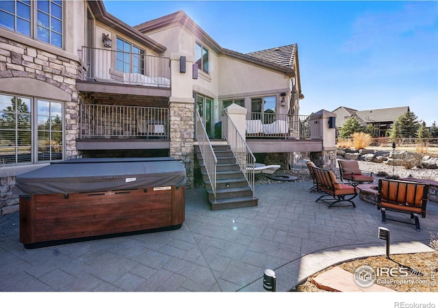 view of patio with stairway, a hot tub, and a balcony