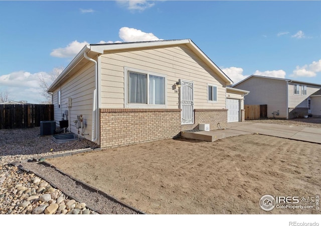 view of front facade with brick siding, fence, concrete driveway, cooling unit, and a garage