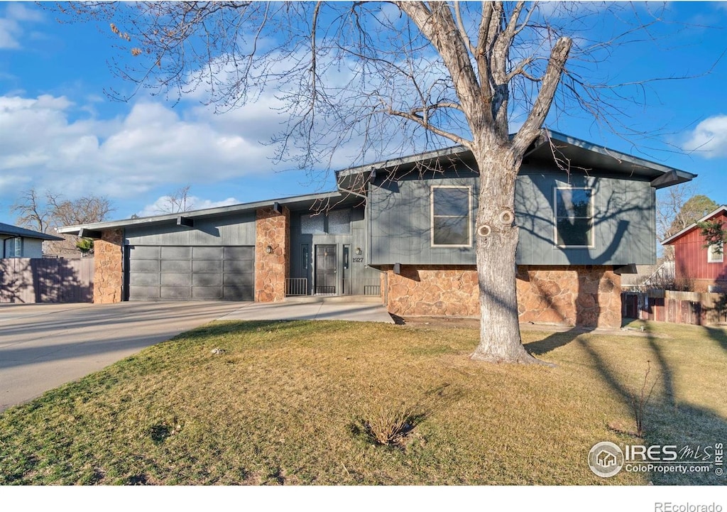 tri-level home with a front yard, fence, driveway, stone siding, and a garage