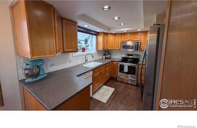 kitchen featuring dark countertops, backsplash, appliances with stainless steel finishes, a peninsula, and a sink