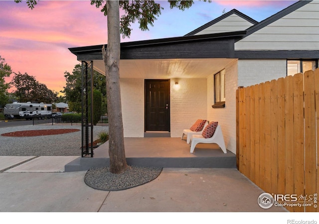 view of exterior entry featuring brick siding and fence