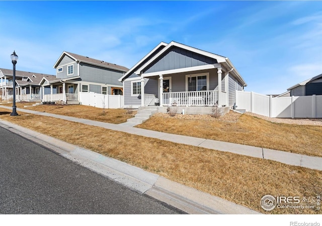 view of front of house with board and batten siding, covered porch, a front yard, and fence