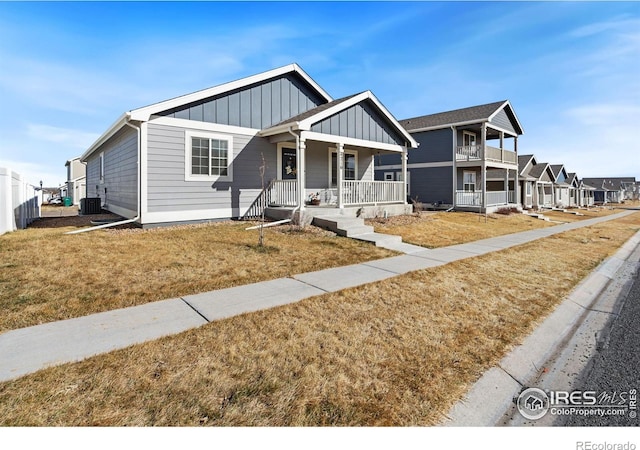 view of front facade with board and batten siding, a front yard, central AC unit, and covered porch