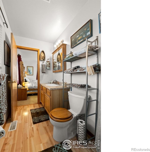562 E St, Hillrose, CO 80733 - ensuite bathroom with vanity, connected bathroom, toilet, visible vents, and wood finished floors