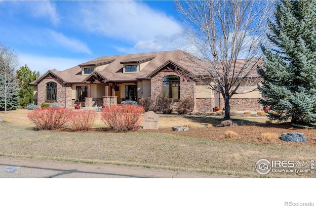 view of front of home featuring a front yard, stucco siding, stone siding, and a tiled roof