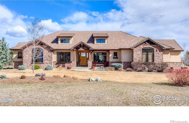 view of front facade with a front yard, stucco siding, a tile roof, and stone siding