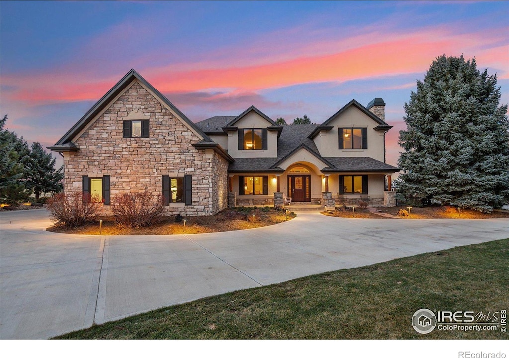 view of front of house featuring stucco siding, a chimney, stone siding, and curved driveway