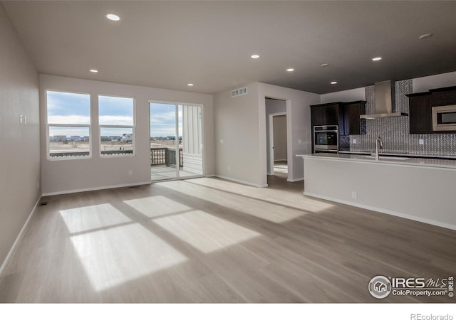 kitchen featuring a sink, light wood-style floors, stainless steel microwave, wall chimney exhaust hood, and tasteful backsplash
