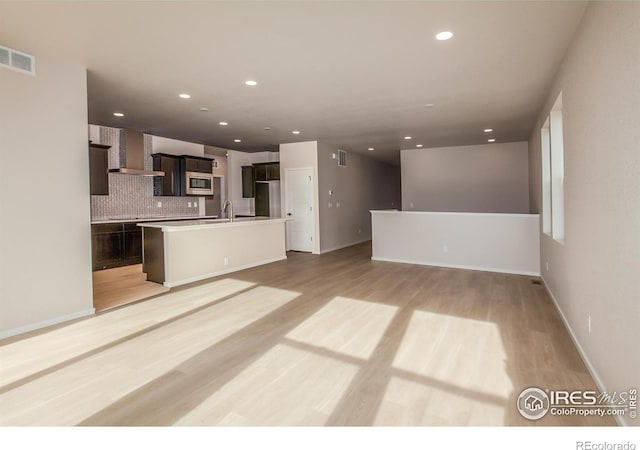 kitchen featuring stainless steel microwave, visible vents, wall chimney range hood, light wood-type flooring, and decorative backsplash