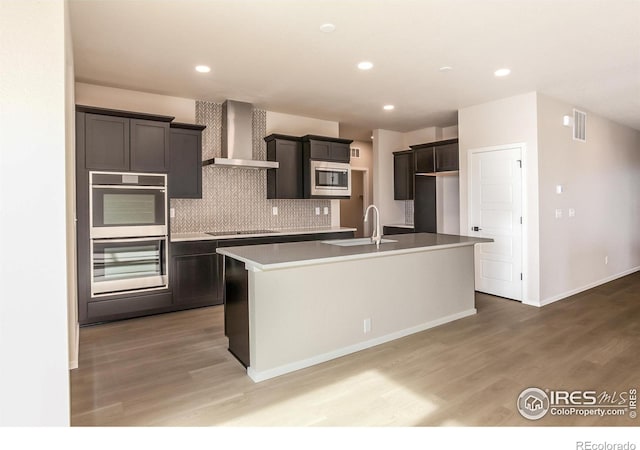 kitchen with visible vents, a kitchen island with sink, a sink, appliances with stainless steel finishes, and wall chimney range hood