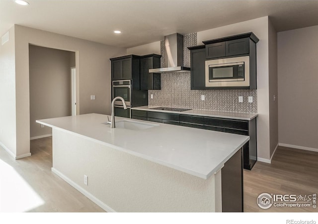 kitchen with light wood-style flooring, a sink, decorative backsplash, appliances with stainless steel finishes, and wall chimney exhaust hood