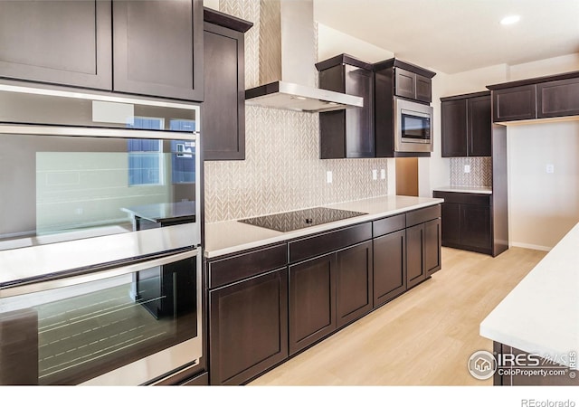 kitchen featuring stainless steel appliances, dark brown cabinetry, light countertops, and wall chimney range hood