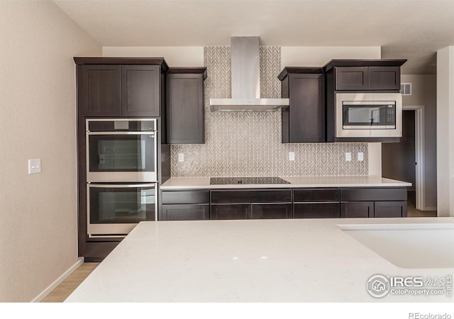 kitchen featuring tasteful backsplash, appliances with stainless steel finishes, wall chimney exhaust hood, and light countertops