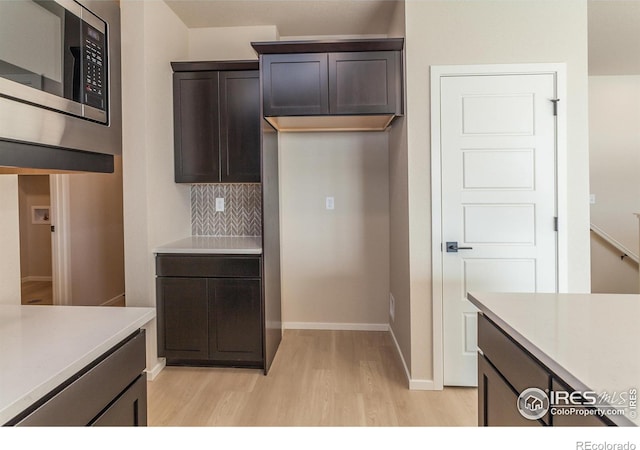 kitchen featuring stainless steel microwave, dark brown cabinetry, light countertops, decorative backsplash, and light wood-style flooring