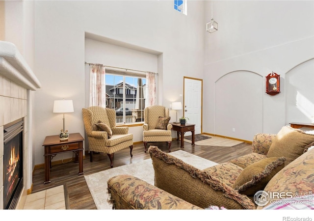 living room with a tiled fireplace, a high ceiling, and wood finished floors
