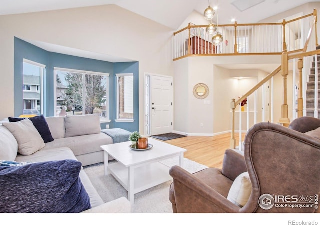 living area with baseboards, high vaulted ceiling, wood finished floors, and stairs