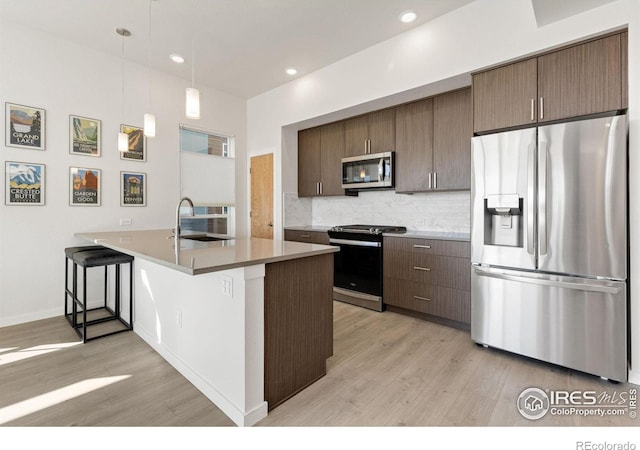 kitchen featuring a sink, stainless steel appliances, light wood-style flooring, and decorative backsplash