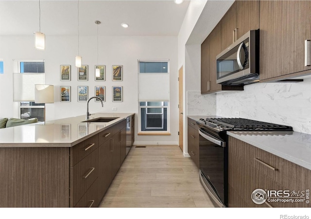 kitchen featuring a sink, stainless steel appliances, light countertops, light wood-style floors, and backsplash