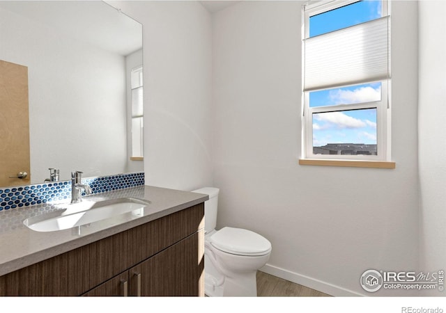 half bath featuring vanity, toilet, wood finished floors, and baseboards