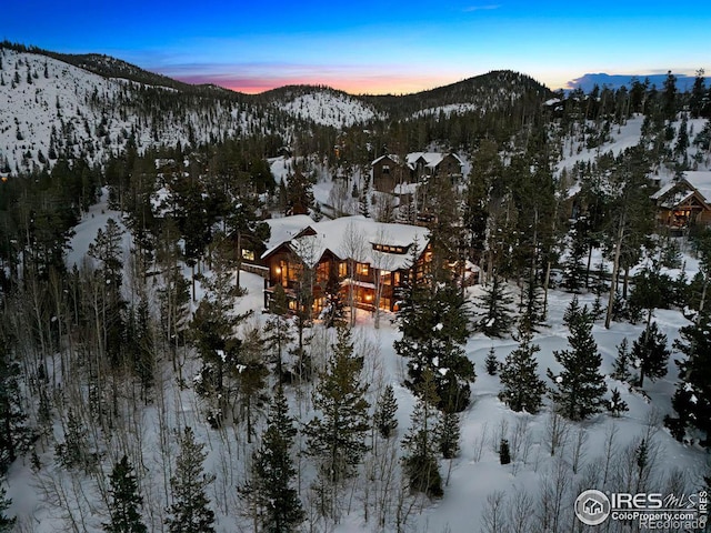 snowy aerial view featuring a wooded view and a mountain view