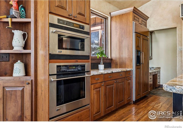 kitchen with light stone counters, brown cabinetry, dark wood-style floors, stainless steel double oven, and open shelves