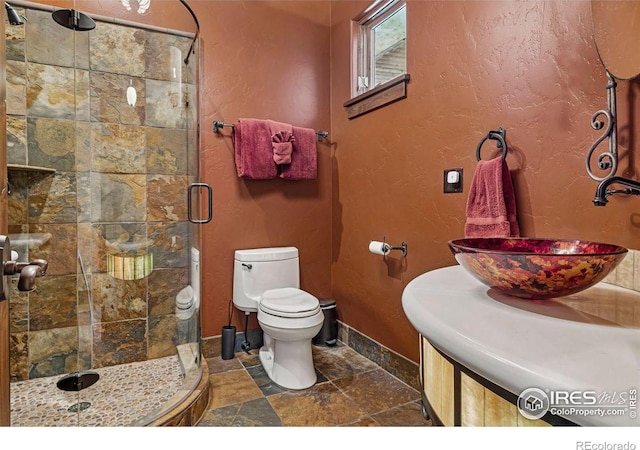 full bath with toilet, stone tile flooring, a shower stall, baseboards, and a textured wall