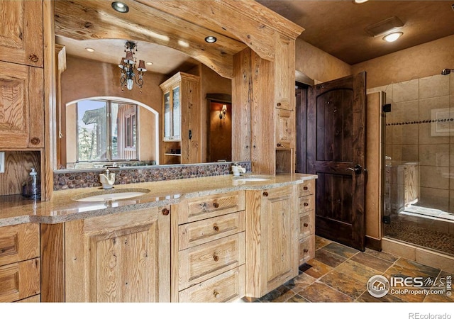 bathroom with a sink, stone tile floors, a shower stall, and double vanity