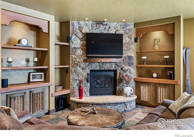 living room with stone finish flooring, built in shelves, a textured ceiling, and a fireplace