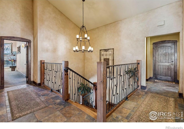 stairs with baseboards, arched walkways, an inviting chandelier, a towering ceiling, and stone tile flooring