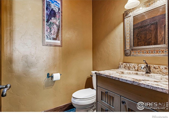 bathroom with toilet, vanity, and a textured wall