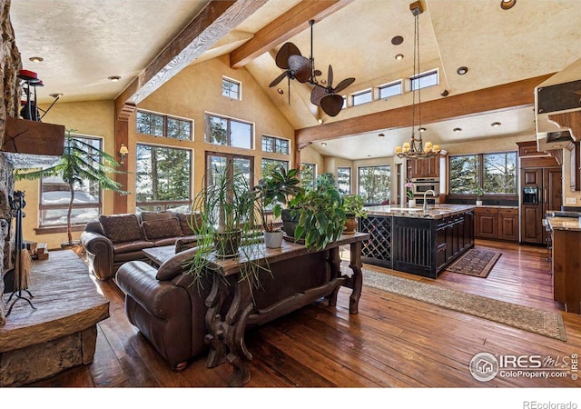 living area with dark wood finished floors, beam ceiling, ceiling fan with notable chandelier, and high vaulted ceiling