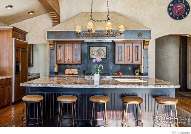 kitchen with glass insert cabinets, dark wood-type flooring, a kitchen breakfast bar, an inviting chandelier, and a sink