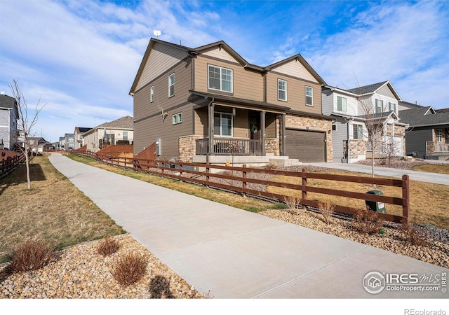 254 Ptarmigan Ln, Johnstown, CO 80534 - view of front of house with a residential view, concrete driveway, a fenced front yard, stone siding, and a porch