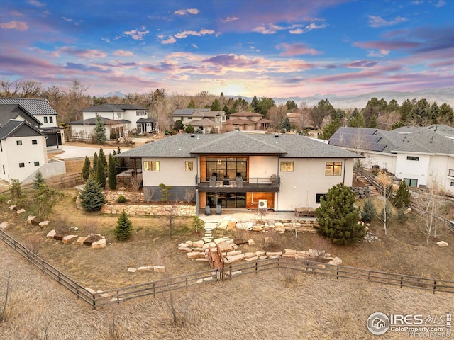 back of property at dusk featuring a fenced backyard, a residential view, and roof with shingles