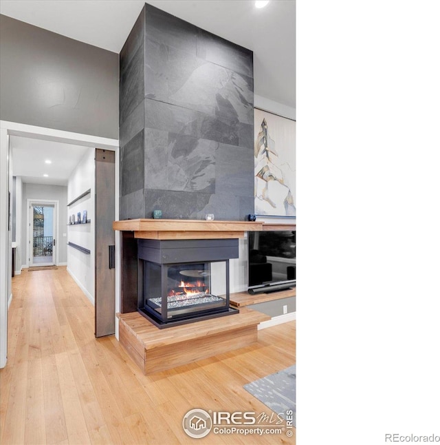 unfurnished living room featuring a multi sided fireplace, wood finished floors, recessed lighting, and baseboards