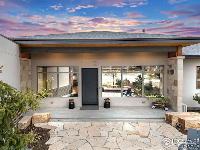 doorway to property with roof with shingles and stone siding