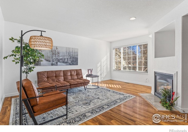 living area with wood finished floors, baseboards, recessed lighting, a tile fireplace, and a textured ceiling