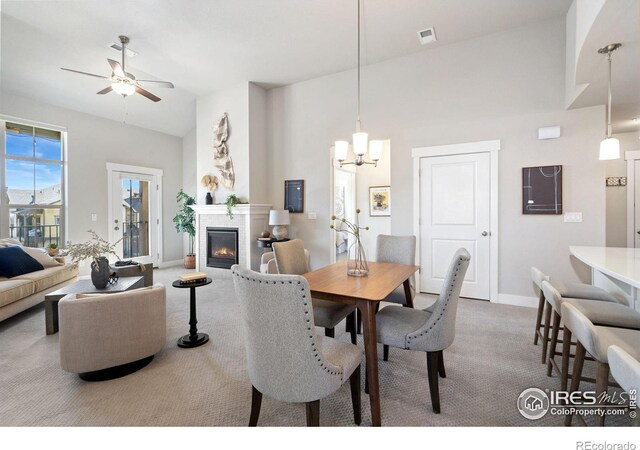 dining area featuring baseboards, carpet floors, ceiling fan with notable chandelier, a glass covered fireplace, and high vaulted ceiling