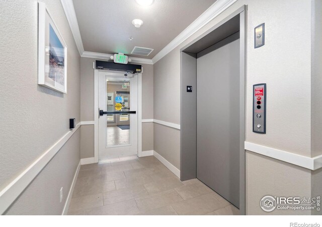 hallway with visible vents, elevator, crown molding, light tile patterned floors, and baseboards