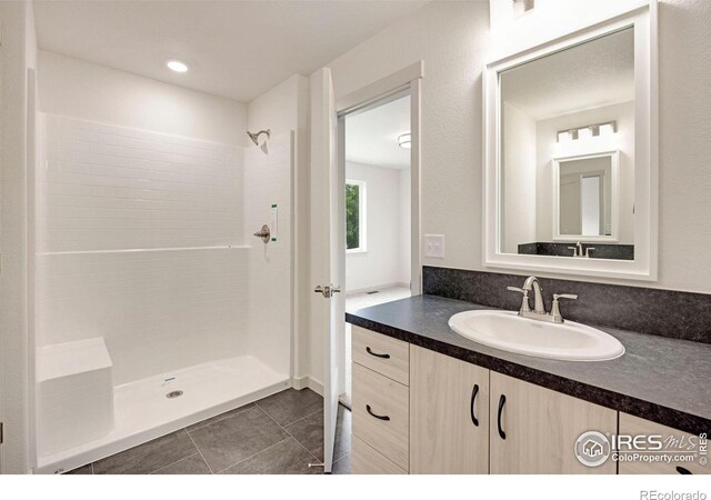 bathroom featuring tile patterned flooring, tiled shower, and vanity
