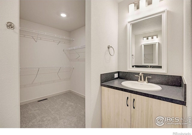 bathroom featuring vanity, a spacious closet, baseboards, and visible vents