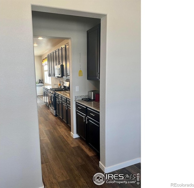 kitchen featuring baseboards, appliances with stainless steel finishes, light stone counters, and dark wood-type flooring