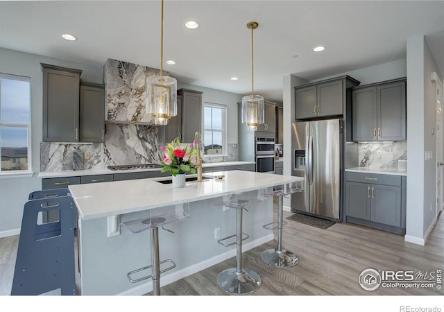 kitchen with stainless steel appliances, a kitchen island with sink, light countertops, and light wood-style flooring